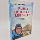 „Fühlt sich nach Leben an“ von Max Baudrexl. Ein Mann in Outdoor-Kleidung, hinreißende Berglandschaft im Hintergrund.