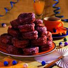 Ein Stapel glasierter Donuts auf einem Tisch, umgeben von einem Saftglas, einer Kaffeetasse und bunten Dekorationen.