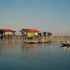 Stelzenhäuser mit bunten Dächern über dem Wasser, Boote im Vordergrund, ruhige Atmosphäre, klarer Himmel.