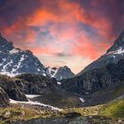 Ein dramatischer, roter Himmel über schneebedeckten, zerklüfteten Berggipfeln bei Sonnenuntergang.