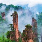 Es sind nebelverhangene, steile Felsformationen mit Pflanzen und grünen Bäumen umgeben von dichtem Wald.