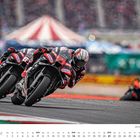 FEBRUAR, ein Kalender mit zwei engen Motorradrennfahrern in Aktion auf einer Rennstrecke, Publikum unscharf im Hintergrund.