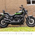 "FEBRUAR" und "Harley-Davidson" auf grünem Tank. Schwarzes Motorrad vor Ziegelwand. Kalender zeigt Februar.