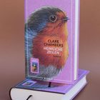 „Clare Chambers Heimliche Zeilen Roman“ auf lila Cover mit Rotkehlchen-Illustration. Buch mit Lesezeichen auf Untergrund.