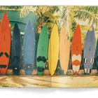 Bunte Surfbretter lehnen an einer Wand, umgeben von Palmenblättern. Die Bretter sind in kräftigen Farben bemalt.