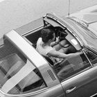 Text "Targa" am Auto. Obenansicht eines klassischen Autos mit offenem Dach, Frau am Steuer.