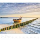 Februar 2027, Am Meer. Ein Holzboot an einem ruhigen Strand neben einer Reihe von Wellenbrechern im Wasser.