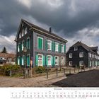 Kalenderblatt Februar 2027, zeigt verschieferte Häuser an einer kopfsteingepflasterten Straße unter wolkenverhangenem Himmel.