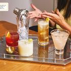 Text: Yuzu-Negroni, Trauben-Soju mit Yakult, Oolong-Highball, Grapefruit-Margarita. Vier Cocktails auf einem silbernen Tablett.