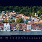 06 Juni. Ein Hafen mit bunten Häusern und Booten, umgeben von grünen Hügeln, vermutlich in Norwegen.