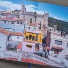 Ein Bild zeigt bunte Häuser vor antiken Ruinen unter blauem Himmel.