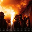 Kalender mit Datum und Wochentagen unten. Feuerwehrleute in Schutzanzügen vor intensiven Flammen.