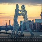 "Molecule Man 2", Kalender mit Monatsübersicht. Silhouette von Figuren im Wasser, Stadtlandschaft im Hintergrund bei Sonnenuntergang.