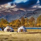 Keine Texte vorhanden. Drei runde, weiße Jurten stehen in einer herbstlichen Landschaft mit Bergen im Hintergrund.