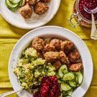 Hackbällchen mit Kartoffelpüree, Gurkenscheiben und Preiselbeeren auf weißen Tellern, gelbes Tischtuch.