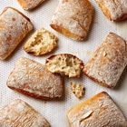Mehrere goldbraune Ciabatta-Brötchen liegen auf einem Backblech mit einem zerbrochenen Brötchen in der Mitte.