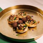 Keine Texte vorhanden. Geröstete Artischockenböden mit Falafel, Pinienkernen und frischen Kräutern auf einem goldenen Tablett.