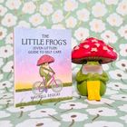 Buch "The Little Frog's (Even Littler) Guide to Self-Care" von Maybell Eequay. Nebenbei steht eine Froschfigur mit Pilzkappe.