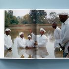 Lienseitentext: "THE W A T." Mehrere Menschen in weißen Gewändern stehen im Wasser für eine religiöse Zeremonie.