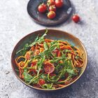 Ein Teller mit Spaghetti, Rucola, Tomaten und Pesto. Im Hintergrund eine Schale mit Cocktailtomaten.