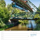 17. Woche April/Mai 2027. Schwebebahn über einem Fluss, umgeben von grünen Bäumen und einer Brücke.