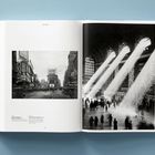 Links ist der Text "New York" oben. Rechts Sonnenstrahlen durch Fenster in einer großen Halle. Links Straßenszene der Stadt.