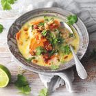 Ein Keramikteller mit einer gelben Suppe, darauf Karotten, Tofu, Koriander und eine Limettenspalte daneben auf einem Tuch.