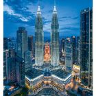 "21 MAI. Mo 24, Di 25, Mi 26, Do 27, Fr 28, Sa 29, So 30. Petronas Towers bei Dämmerung, erleuchtet, vor blauem Himmel."