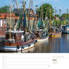19. Woche, Mai 2027. Fischkutter im Hafen von Greetsiel, Niedersachsen. Kutter mit Netzen, Wasser und Gebäude im Hintergrund.