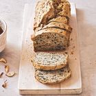 Ein frisch geschnittenes Brot mit Saaten auf einem hölzernen Schneidebrett, daneben eine Schüssel.