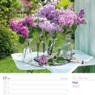 Termineintrag für die 20. Woche im Mai 2027. Fliederblumen in Vasen auf einem Gartentisch.