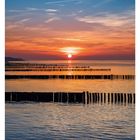 23. Juni, Mo 07, Di 08, Mi 09, Do 10, Fr 11, Sa 12, So 13. Sonnenuntergang am Meer mit Holzpfählen, orange-blauer Himmel.