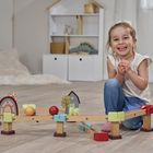 Ein lächelndes Kind sitzt auf dem Boden, spielt mit einer bunten Holzkugelbahn in einem gemütlichen, hellen Raum.