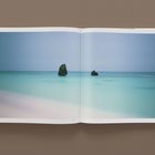 "Seascape, 2003" ist unter einem weiten, ruhigen Meeresbild gedruckt. Ein geöffnetes Buch zeigt türkisblaues Wasser und blauen Himmel.