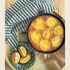 Seite 26. Ein runder Kuchen mit Orangenscheiben, auf einem Tablett, daneben halbierte Orangen auf einem grünen Teller.