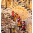 "Wassertragende Frauen auf Treppen von Panna Meena ka Kund bei Jaipur, Indien." Vier Frauen in bunten Kleidern mit Krügen.
