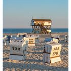Kalenderblatt 27. Juli. Strandkörbe mit Nummern. Pfahlbau am Strand bei Sankt Peter-Ording, blauer Himmel, ruhiges Meer.