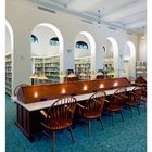 28 JULI. Ein Lesesaal mit Holztischen, Stühlen und Beleuchtung. Im Hintergrund sind Regale mit Büchern zu sehen.