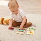 Ein Kleinkind sitzt auf einem Teppich und spielt mit farbigen Holz-Puzzles. Neben ihm liegt ein Kuscheltier.