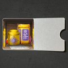 Die gelben Dosen mit violetten Etiketten zeigen weiße Schriftzeichen. Sie sind in einer offenen, hellen Box angeordnet.