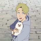 Ein blonder junger Mann hält ein flauschiges, weißes Haustier in der Armgegend einer gepflasterten Straße.