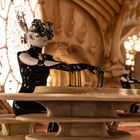 Eine futuristische Szenerie mit einer Person in schwarzem Anzug und optischem Gerät, umgeben von organischen Formen und großen runden Fenstern.