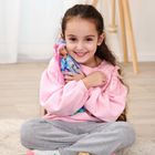 Ein Mädchen in rosa Pullover umarmt eine bunte Puppe, Spielzeug um sie verteilt auf hellem Teppich.