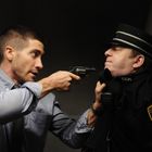 Ein Mann in Hemd bedroht Uniformierten mit Revolver. Aufschrift „Trainman CCR“ auf Uniform. An Schaltpult angenähert.