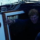 Zwei Anzeigen zeigen "WIND SPEED" und "APPARENT". Ein Mann mit nassen Haaren kämpft mit Sturm auf einem Segelboot.