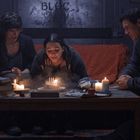 Verschwommenes "BLOC" an der Wand. Eine Frau bläst Kerzen auf einem Kuchen aus, umgeben von zwei Personen, entspannt auf Sofa.