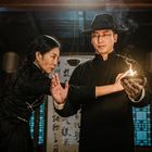 Zwei Personen in traditioneller Kleidung, eine Frau und ein Mann mit Hut, halten eine brennende Lampe, umgeben von Kalligrafien.