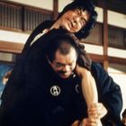 Ein Mann hebt einen anderen in einem Kampf in einem traditionellen japanischen Raum. Konzentrierte Gesichtsausdrücke.