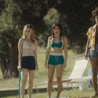 Drei Frauen stehen im Freien auf einer Wiese, mit Liegestühlen im Hintergrund, umgeben von Bäumen.