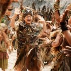 Person in aufwendigem Kostüm aus Naturmaterialien, umgeben von tanzenden Menschen in festlicher Stimmung.